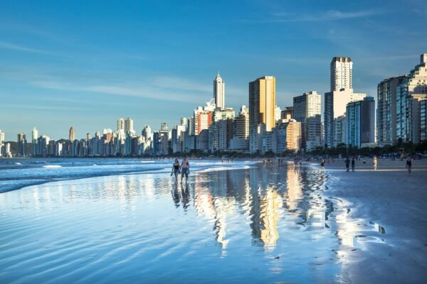 Horizonte promissor: investimentos imobiliários em Santa Catarina movimentam bilhões e atraem investidores Stunning view of Balneário Camboriú's modern skyline reflecting on the beach at daytime.